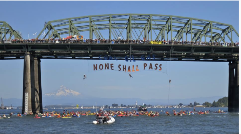 A public demonstration on a bridge, featuring a hanging sign that reads in all-caps, "None shall pass".